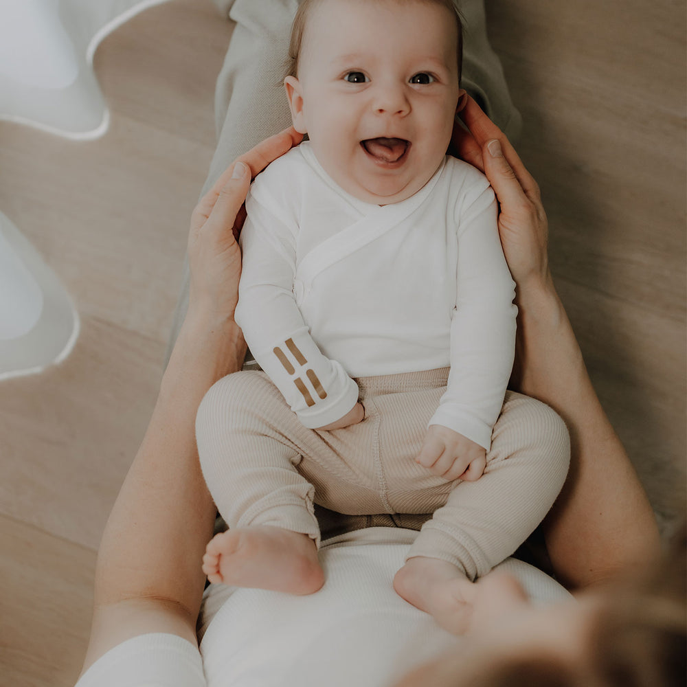 Baby sitzt auf dem Schoß und trägt weißen TRUSTGARN Body aus hautfreundlichem Stoff für empfindliche Haut
