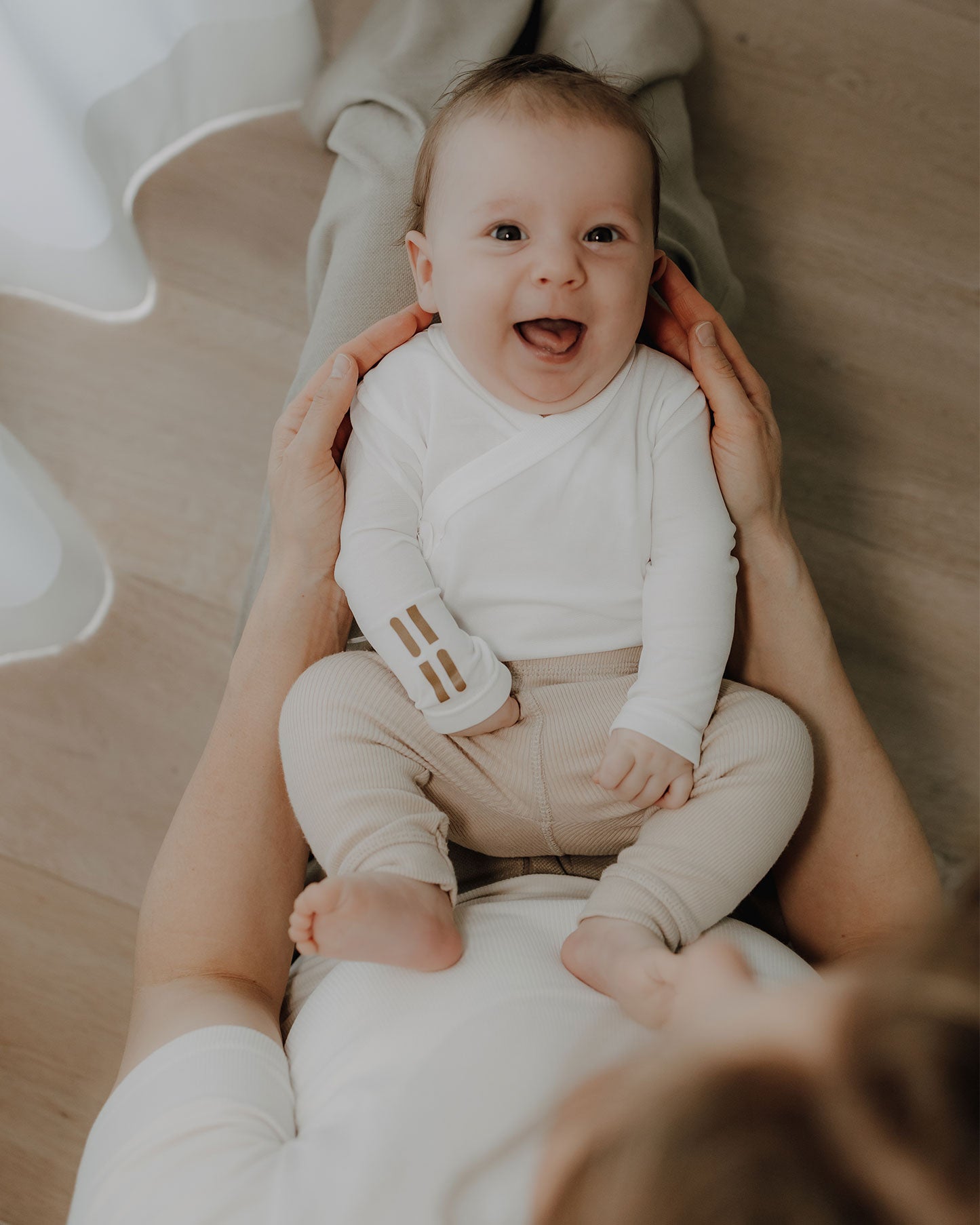 Baby sitzt auf dem Schoß und trägt weißen TRUSTGARN Body aus hautfreundlichem Stoff für empfindliche Haut